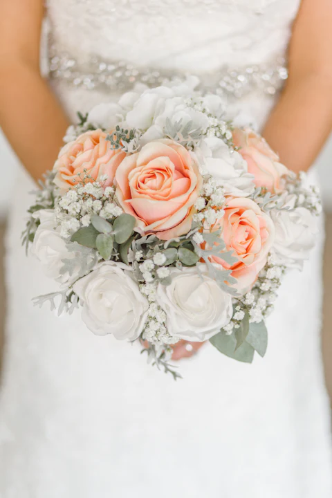 Bride holding a round bouquet of peach and white roses with baby's breath