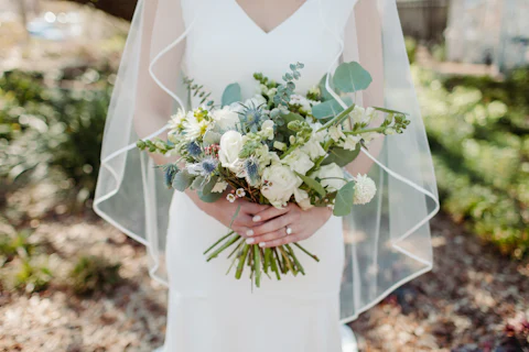 Bride in a veil holding a loose white and green bouquet outdoors