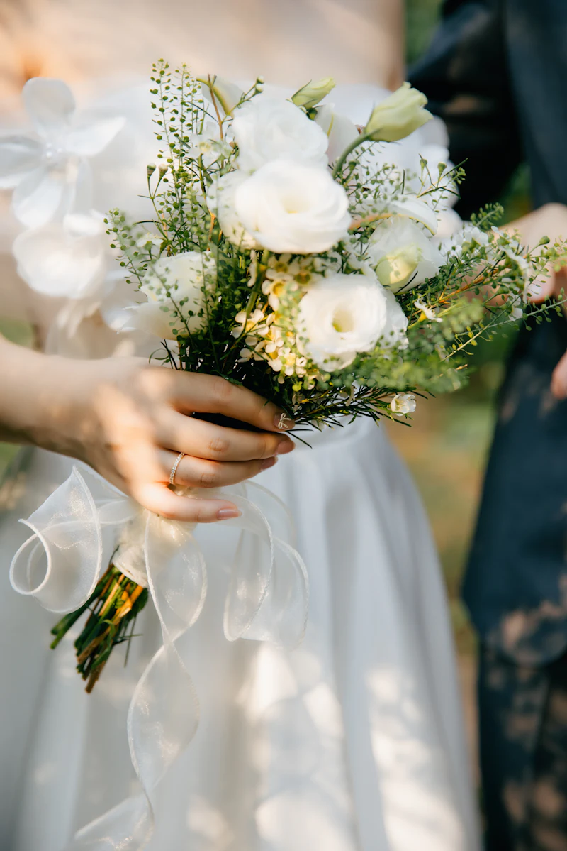 Bride holding a white bouquet with greenery and ribbon