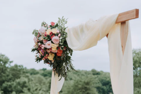 Wooden ceremony arch draped in white fabric with a cascade of roses and greenery