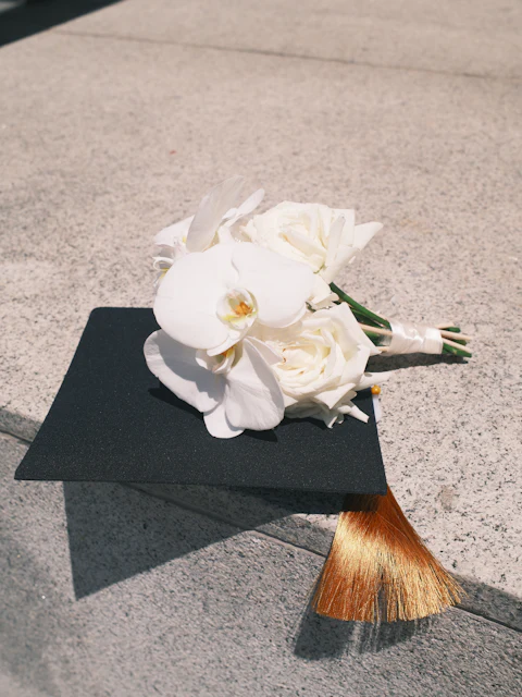 White orchid and rose bouquet resting on a black graduation cap