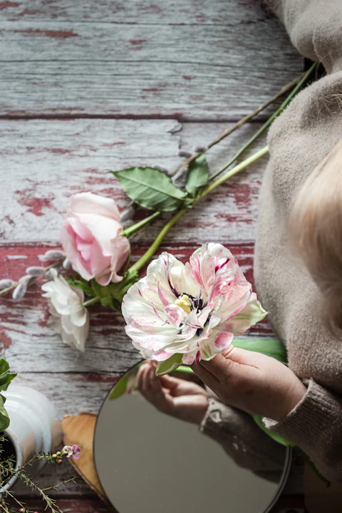 Hand holding a pink and white flower over a weathered wood table