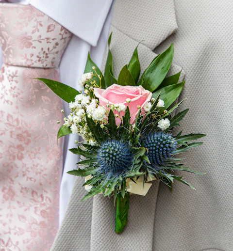 Pink rose and blue thistle boutonniere on a beige suit
