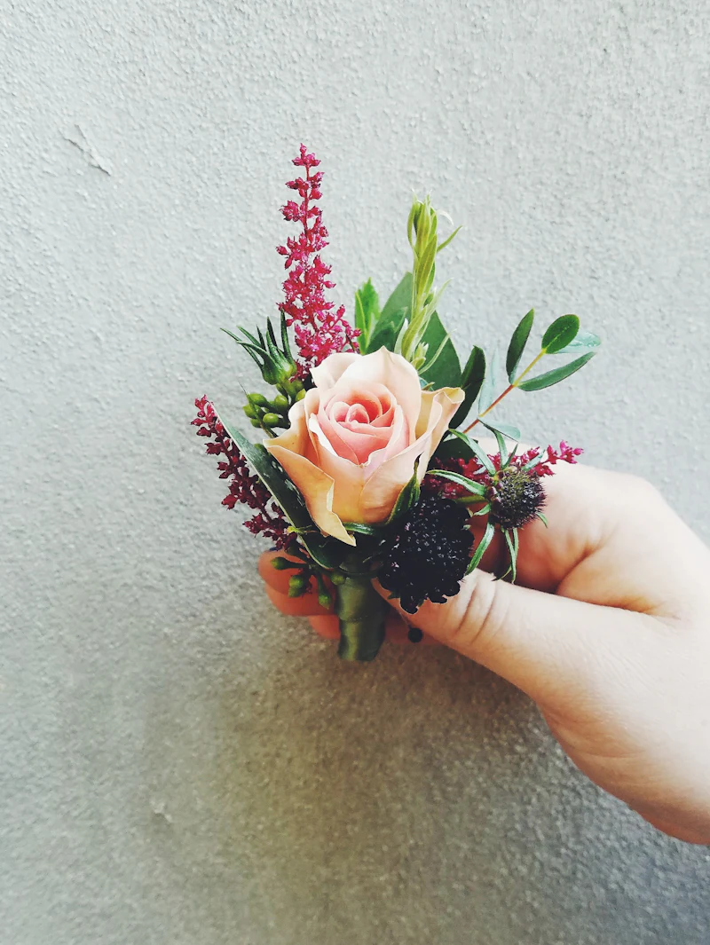 Hand holding a pink rose and heather boutonniere