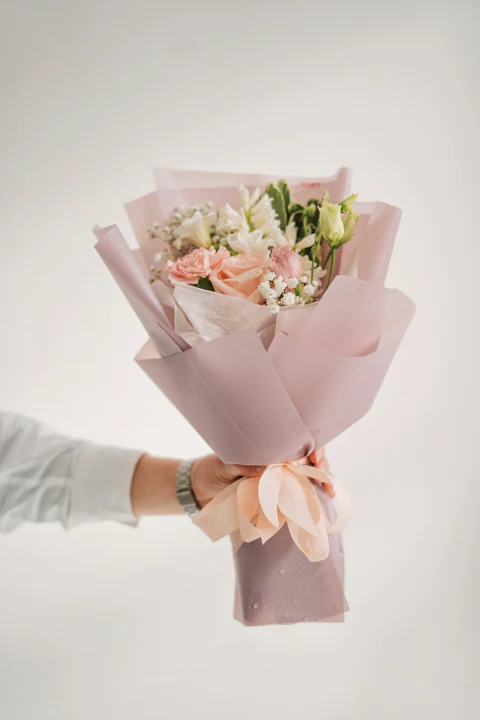Hand holding a small blush bouquet wrapped in pink paper with a ribbon