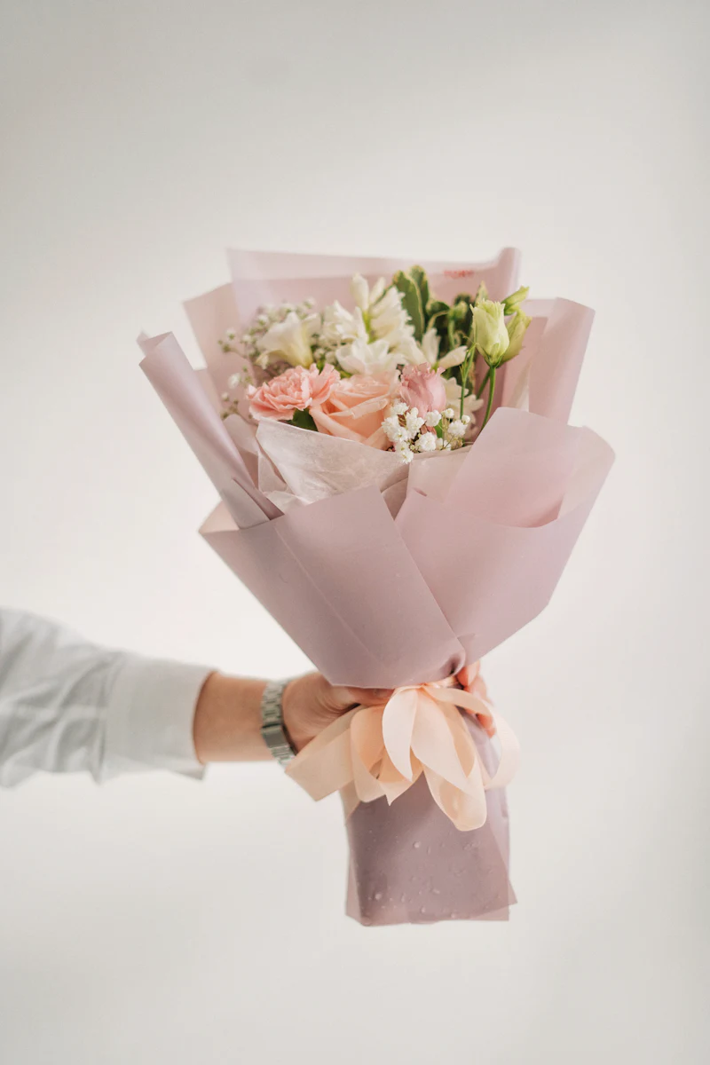 Hand holding a small blush bouquet wrapped in pink paper with a ribbon