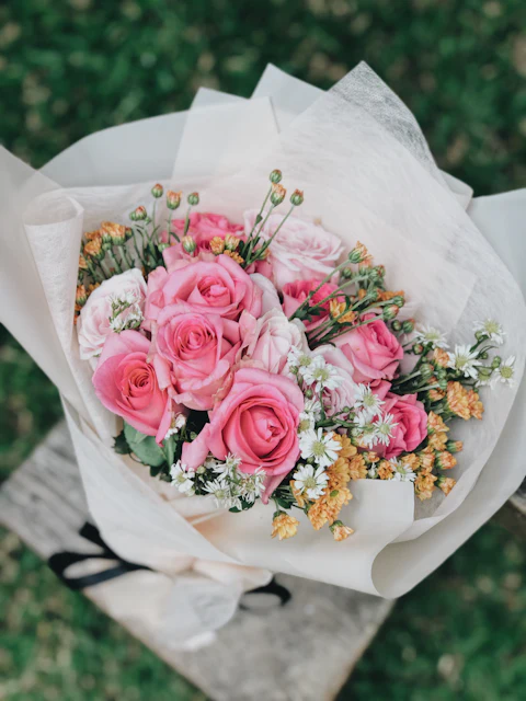 Pink roses with small orange and white flowers wrapped in white paper
